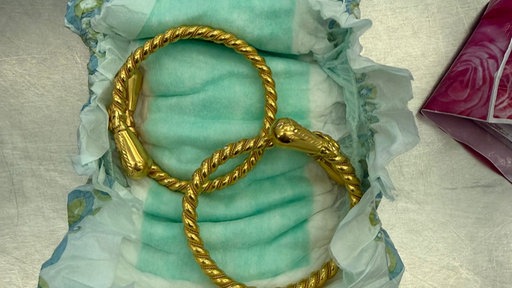 Zwei goldene Ohrringe liegen in einer aufgefalteten Babywindel.