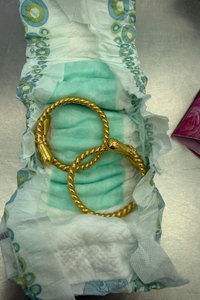 Zwei goldene Ohrringe liegen in einer aufgefalteten Babywindel.