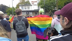 Mehrere Menschen laufen mit Regenbogenflagge durch die Straße