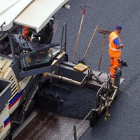 Ein Bauaerbeiter steht auf einem Asphaltfertiger 