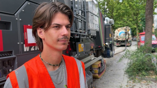 Ein Mann in einer orangenen Warnweste steht vor einem großen Fahrzeug 