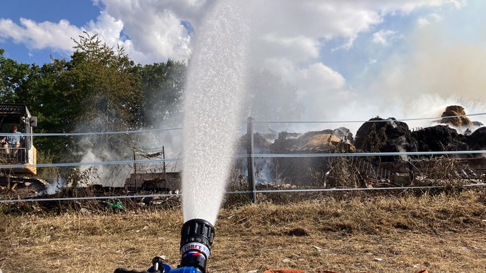 Ein Löschhahn wirft eine Wasserfontäne auf die glühenden Überreste einer Scheune.