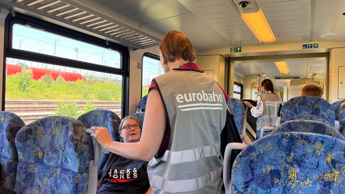 Eine Mitarbeiterin der Eurobahn spricht im Zug mit einer Frau.
