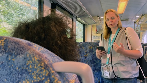 Eine Mitarbeiterin der Eurobahn spricht im Zug mit einer Frau, die von hinten zu sehen ist.