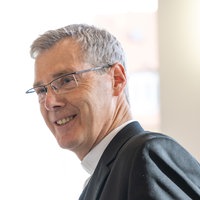 Heiner Wilmer schaut lächelnd vor einem hellen Hintergrund.