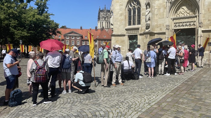 Menschen stehen in einer Schlange aufgereiht vor dem Dom in Münster