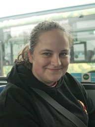 Eine Hundebesitzerin sitzt im Bus und lächelt in die Kamera.