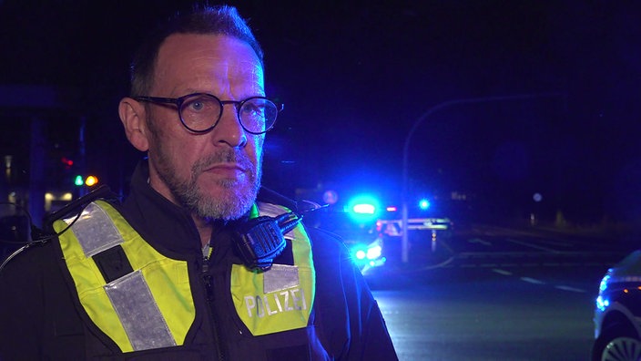 Hauptkommissar Peter Lefering vor einem Polizeiwagen mit Blaulicht