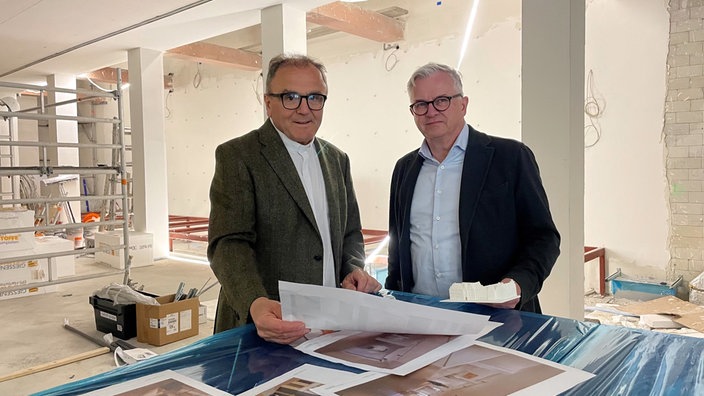 Domprobst Hans-Bernd Köppen und Architekt Jörg Preckel stehen nebeneinander auf einer Baustelle. 