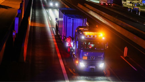 Ein LKW mit besonderem Anhänger fährt mit starker Beleuchtung auf einer nächtlichen Autobahn