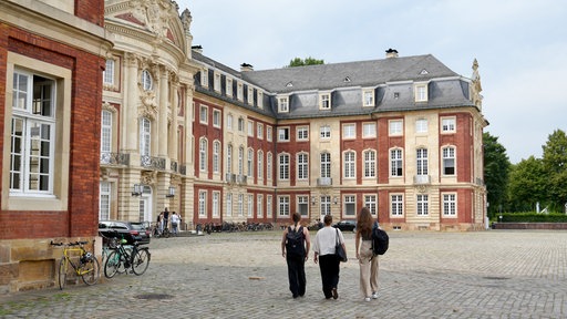 Drei Studentinnen gehen auf das Universitäts-Schloss Münster zu.