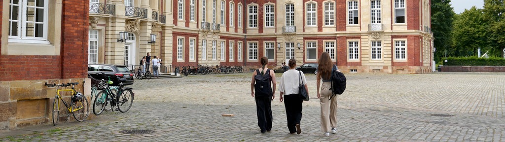 Drei Studentinnen gehen auf das Universitäts-Schloss Münster zu.