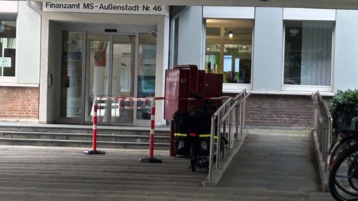 Ein roter Briefkasten vor dem Finanzamt, der von Absperrbändern verdeckt wird