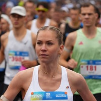 Eine Marathon-Läuferin mit weißem Tanktop läuft an der Kamera vorbei. Hinter ihr sind viele andere Läufer zu sehen.