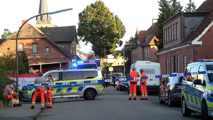Mehrere Einsatzkräfte und Einsatzwägen stehen an einer Straße. Davor ist Flatterband gepannt.