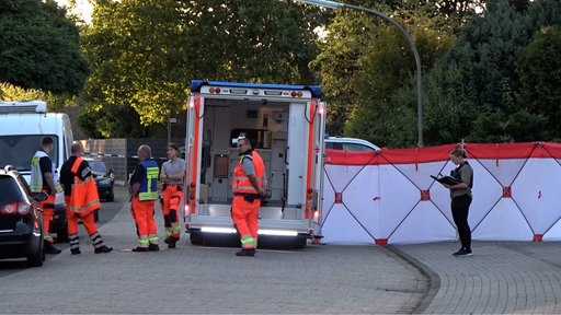 Neben einem Rettungswagen, an dem Einsatzkräfte stehen, wurde ein Sichtschutz aufgebaut.
