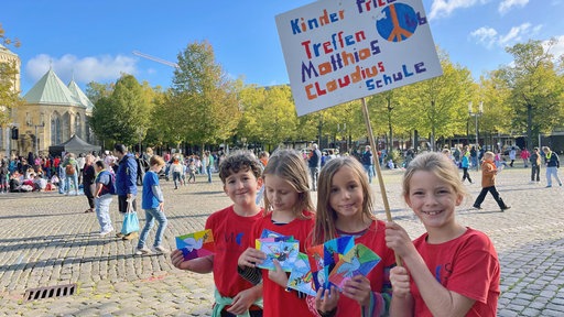 4 SchülerInnen halten ein Schild hoch mit der Aufschrift: Kinder-Friedenstreffen. Matthias-Claudius-Schule.