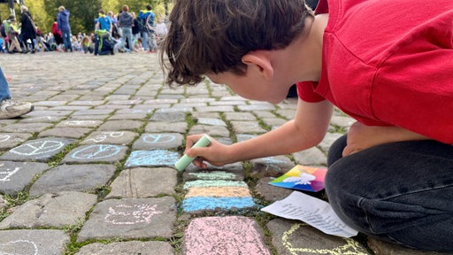 Ein Schüler malt mit Kreide auf dem Kopfsteinpflaster des Domplatzes.