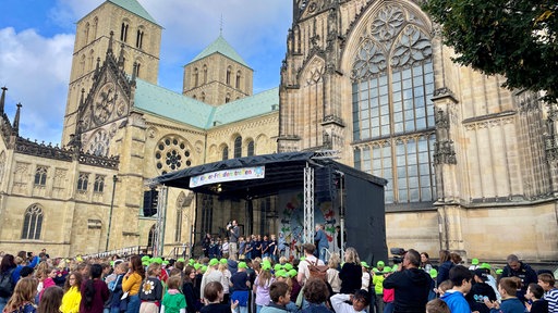 Viele Schüler haben sich vor einer Bühne auf dem Domplatz versammelt.
