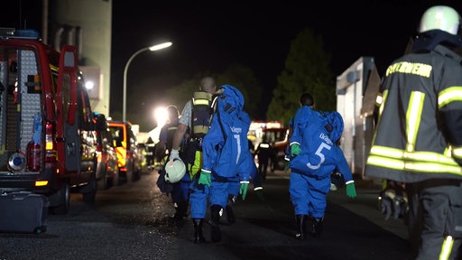 Einsatzkräfte in Schutzanzügen laufen zwischen den Einsatzwägen.