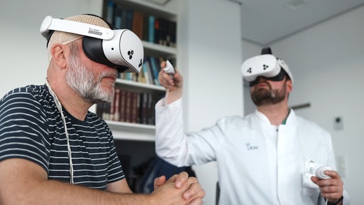 Alexander Ewen (l.) ist Glioblastom-Langzeitüberlebender. Er lässt sich von Prof. Markus Holling anhand von MRT-Bildern in der VR-Brille virtuelle Eindrücke seines Gehirns zeigen.