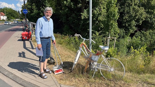 Ein lächelnder Mann mit einem Kehrblech neben einem weißen Fahrrad.