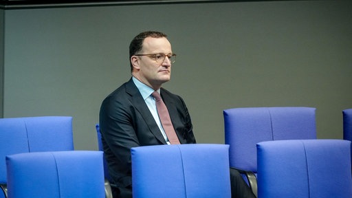 Jens Spahn sitzt im Bundestag, vor ihm sind die Stuhlreihen leer