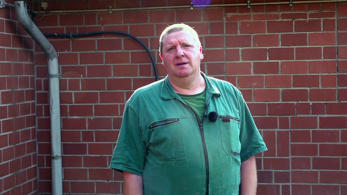 Schweinehalter Thomas Ostendorf steht vor einer roten Backsteinwand und schaut in die Kamera.