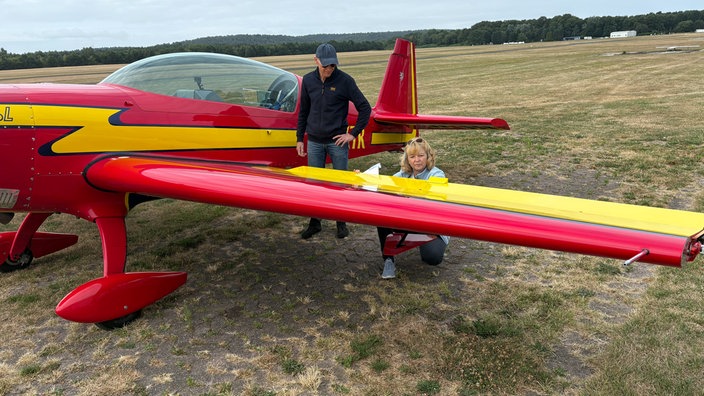 Eine Frau und ein Mann stehen neben einem Flugzeug und schauen auf einen der Flügel.