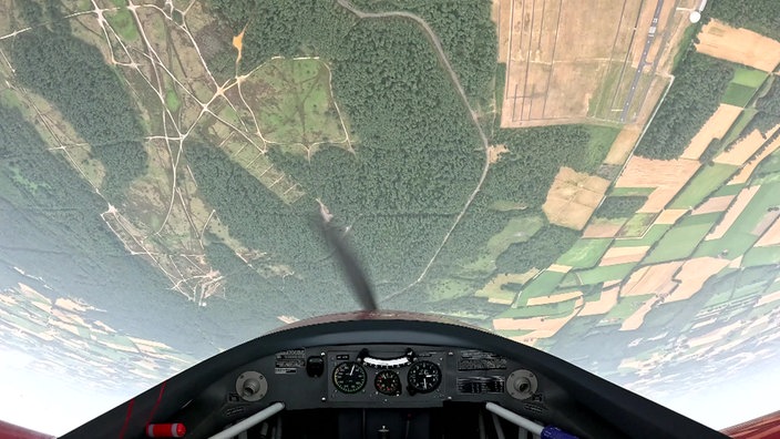 Ein Kleinflugezug fliegt über Kopf, über dem Cockpit sind Felder zu sehen.