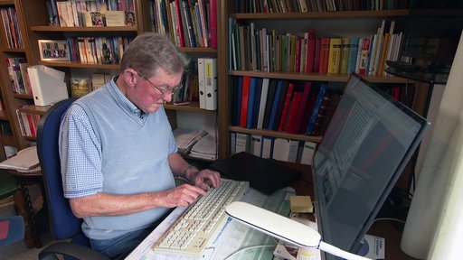 eine Person an einem Computer vor einer Bücherregalwand