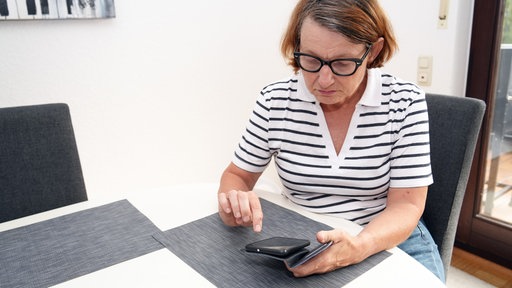 Eine Frau, die an einem Tisch ihr Handy bedient.
