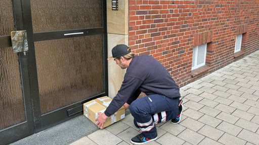 Ein Mann hebt ein Paket vor einer Haustür hoch.