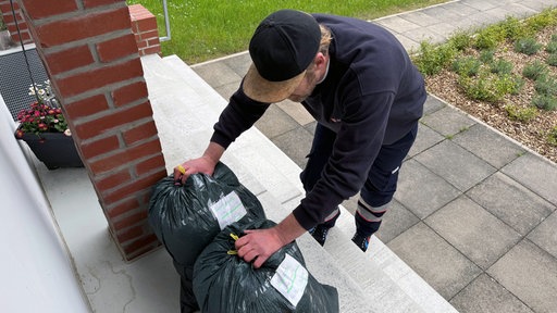 Ein Mann greift nach zwei Altkleidersäcken.