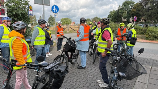 Eine Gruppe Senioren mit E-Bikes und Warnwesten hört einer Polizistin zu.