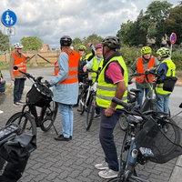 Eine Gruppe Senioren mit E-Bikes und Warnwesten hört einer Polizistin zu.