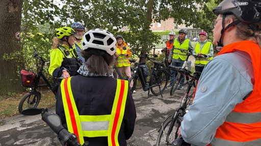 Eine Gruppe Senioren steht mit ihren E-Bikes zusammen und erhält von einer Polizistin eine Einweisung.