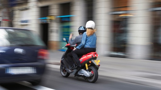 Zwei Personen fahren auf einem Motorroller