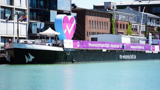Die MS Wissenschaft liegt am Hafen in Münster. Auf dem Schiff steht ein großes Herz.