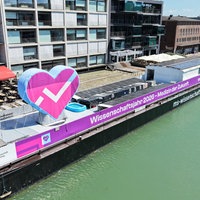 Die MS Wissenschaft liegt am Hafen Münster. An der Seite des Schiffs hängt ein großes Banner mit der Aufschrift "Wissenschaftsjahr 2026".