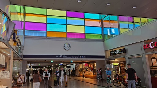 Hauptbahnhof Münster von innen richtung Gleise, obere Fensterfront ist mit bunten Gläsern versehen 