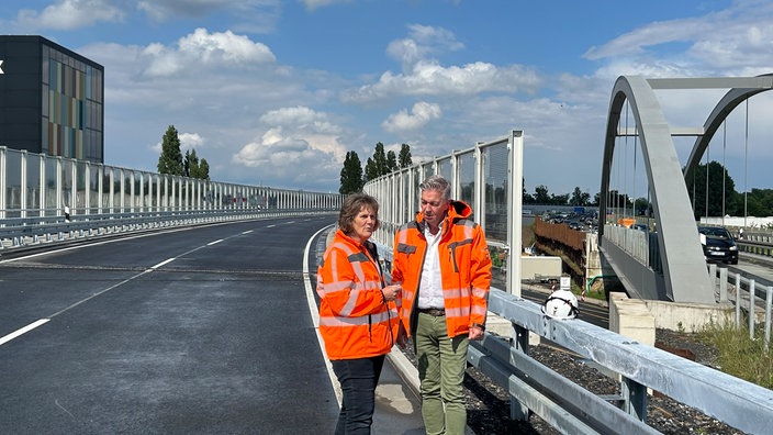 Zwei Menschen in Warnkleidung stehen auf der neuen Brücke der B51.
