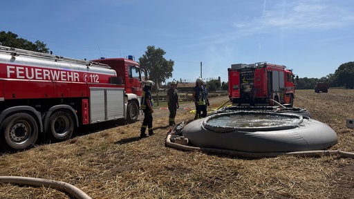 Feuerwehrmänner stehen um ein mobiles Löschbecken herum, aus dem sie Wasser durch Schläuche entnehmen.