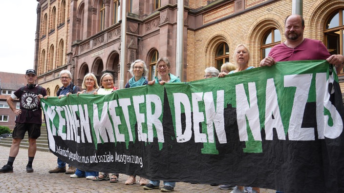 Mehrere ältere Menschen halten vor dem Landgericht Münster ein Banner hoch mit der Aufschrift "Keinen Meter den Nazis".