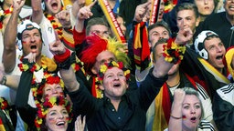 Ausschnitt von einer jubelnden Menge an Menschen beim Public Viewing. Alle tragen deutsche Fußball-Fanartikel wie Fußballtrikots oder Blumenketten in schwarz, rot, gelb.