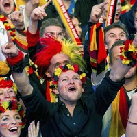 Ausschnitt von einer jubelnden Menge an Menschen beim Public Viewing. Alle tragen deutsche Fußball-Fanartikel wie Fußballtrikots oder Blumenketten in schwarz, rot, gelb.