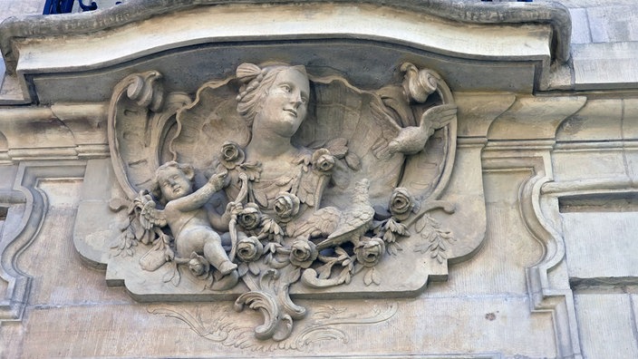 Aufnahme von Kunstvollem Fassadenbild aus Sandstein. Es ist zum Beispiel ein Frauenkopf und ein Engel zu sehen.