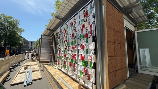 An der Wand des Recycling-Pavillons sind alte Werbeplanen angebracht.