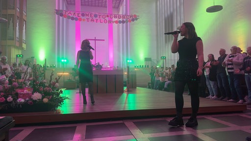 Zwei Sängerinnen singen in einer bunt beleuchteten Kirche.