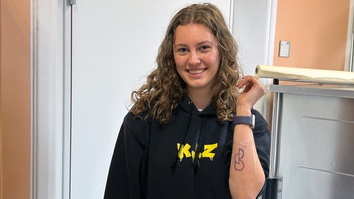 Eine Frau zeigt ihr frisch gestochenes Organspendertattoo